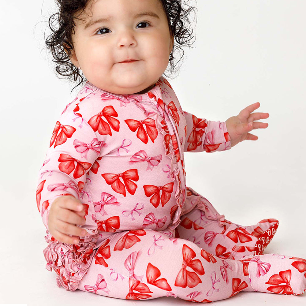 Baby wearing a pink outfit with red bow patterns on a white background