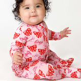 Baby wearing a pink outfit with red bow patterns on a white background