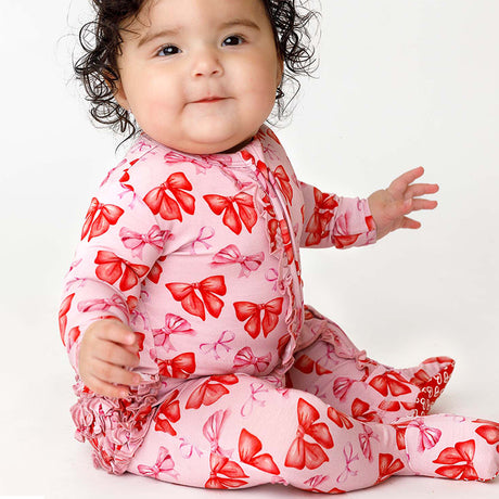 Baby wearing a pink outfit with red bow patterns on a white background