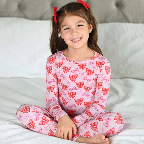 Young girl wearing pink bow patterned pajamas sitting on a bed.