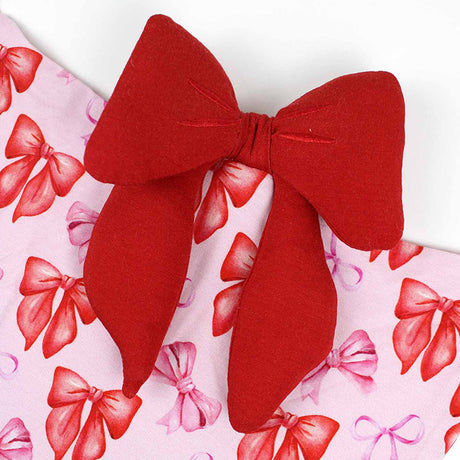Red bow attached to a blanket on a pink background with red bows.