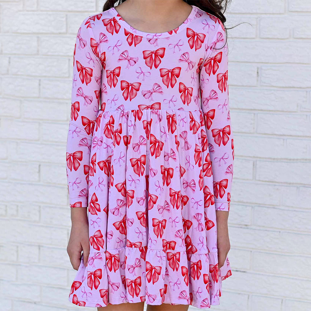 Pink dress with red bow pattern worn by a person against a white brick wall.