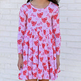 Pink dress with red bow pattern worn by a person against a white brick wall.