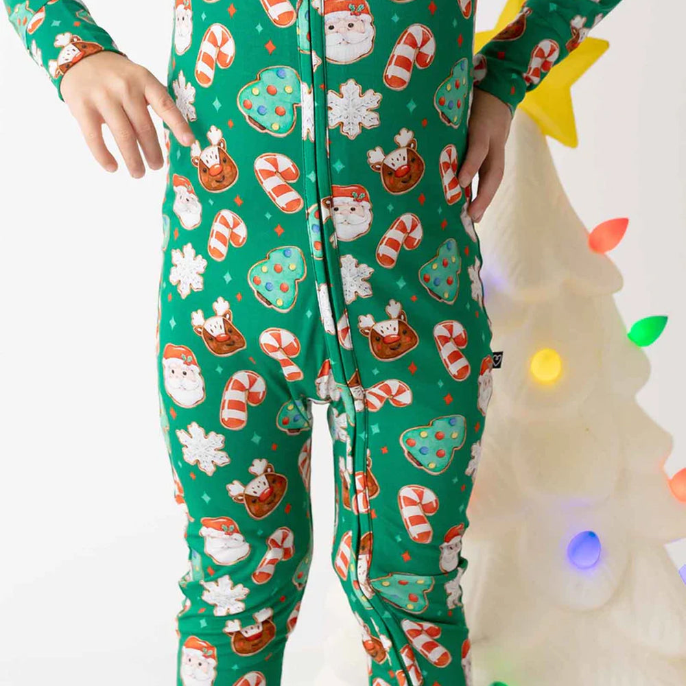 Child wearing festive pajama pants with Christmas-themed pattern in front of a decorated tree.
