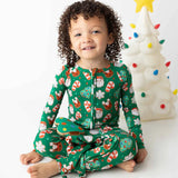 Child wearing festive green pajamas with Christmas patterns, sitting in front of a decorated Christmas tree.