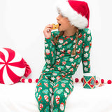 Child wearing a green Christmas pajama set with Santa Claus pattern, eating a cookie.