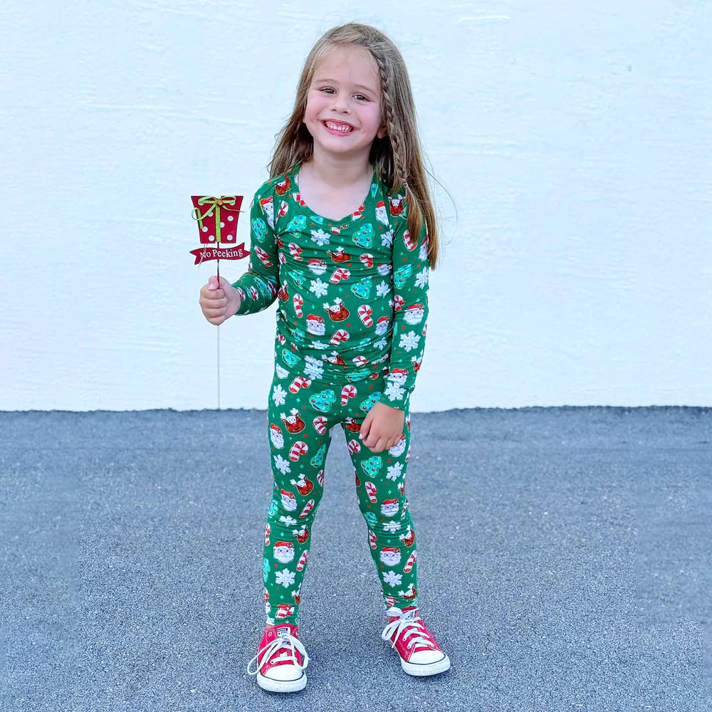 Child wearing a green Christmas-themed pajamas holding a small candy cane flag.