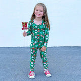Child wearing a green Christmas-themed pajamas holding a small candy cane flag.