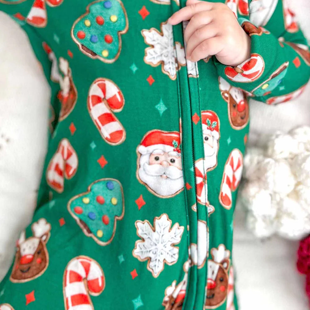Green onesie with Christmas-themed pattern featuring Santa Claus, reindeer, and cookies.
