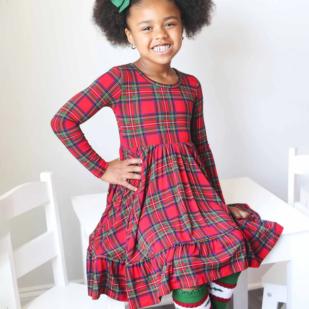 Child wearing a red plaid dress sitting on a white chair.