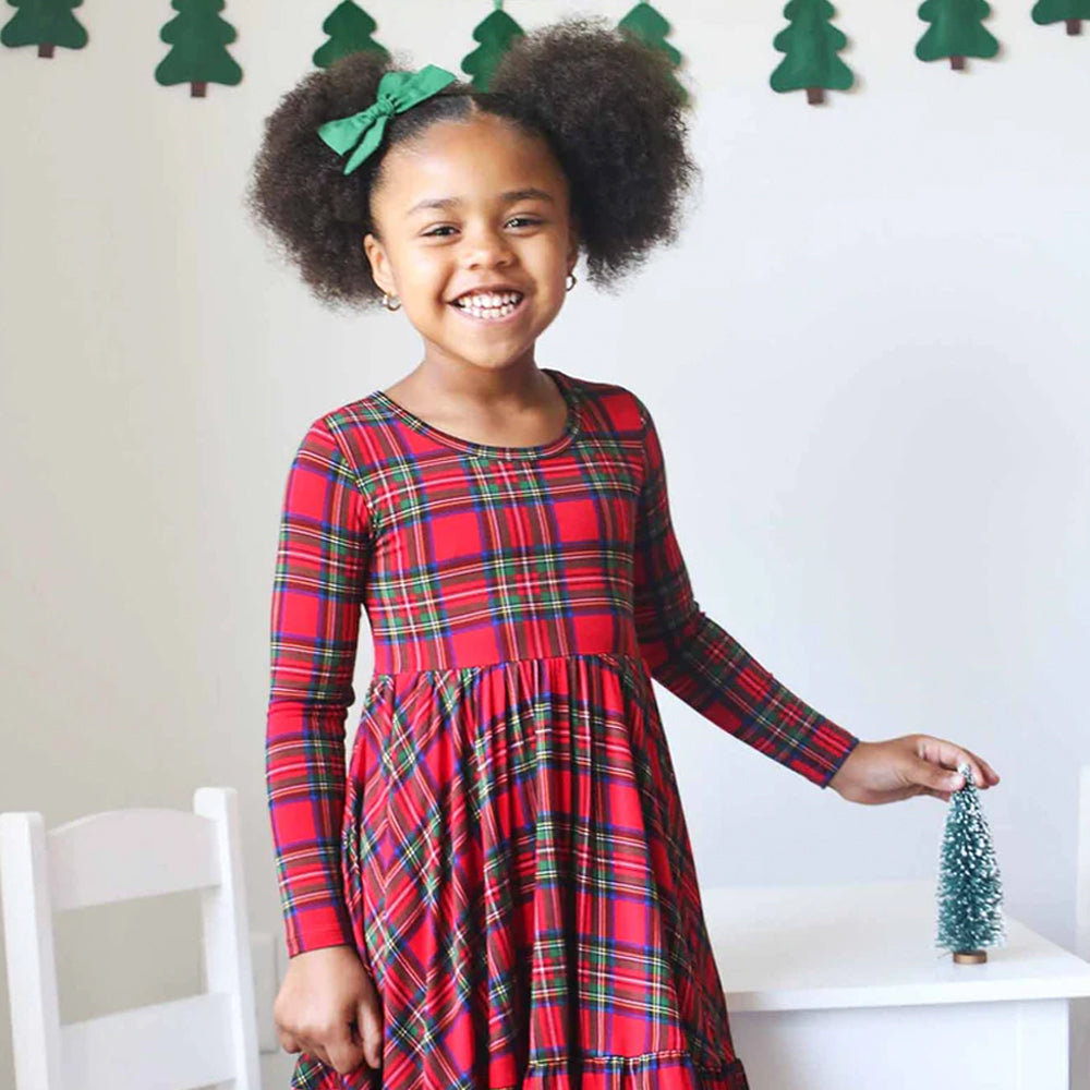 Young girl in a red plaid dress standing in a room with Christmas decorations.