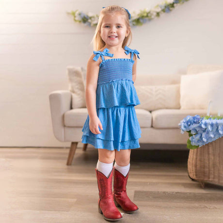 Young girl in a blue dress and red boots standing in a living room.