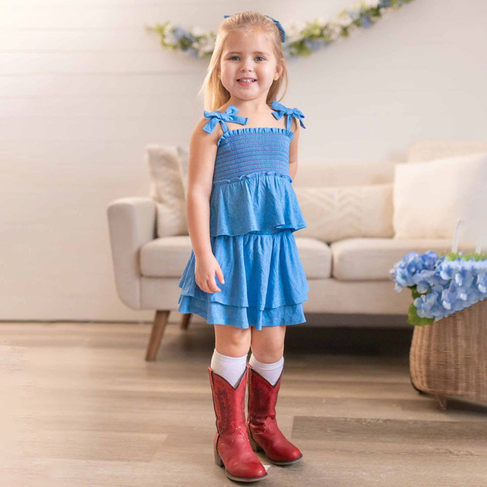 Young girl in a blue dress and red boots standing in a living room.
