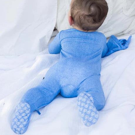 Baby wearing a blue onesie with white sole shoes on a white blanket