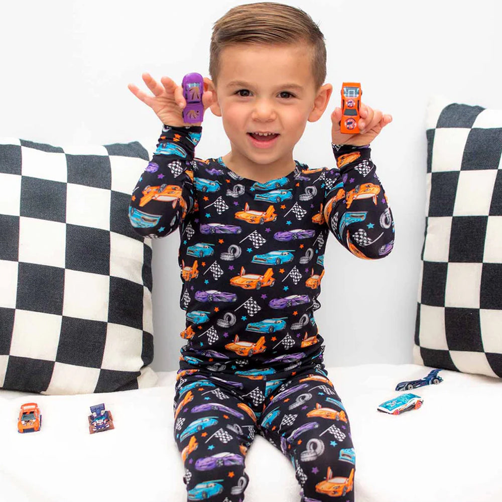 Child wearing a car-themed pajama set with checkered pillows in the background