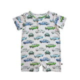 A close-up of a short-sleeve baby romper or bodysuit with an all-over vintage car print on a light cream background. The print features retro cars in light blue, medium blue, green, and white, with a buttoned chest pocket.