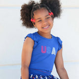 A young girl with curly hair wearing a bright blue sleeveless top with 'USA' printed on the front, smiling against a light background.