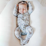 Baby sleeping in a ergonomic positioning device with a patterned onesie.