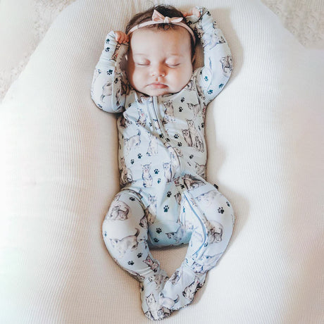 Baby sleeping in a ergonomic positioning device with a patterned onesie.