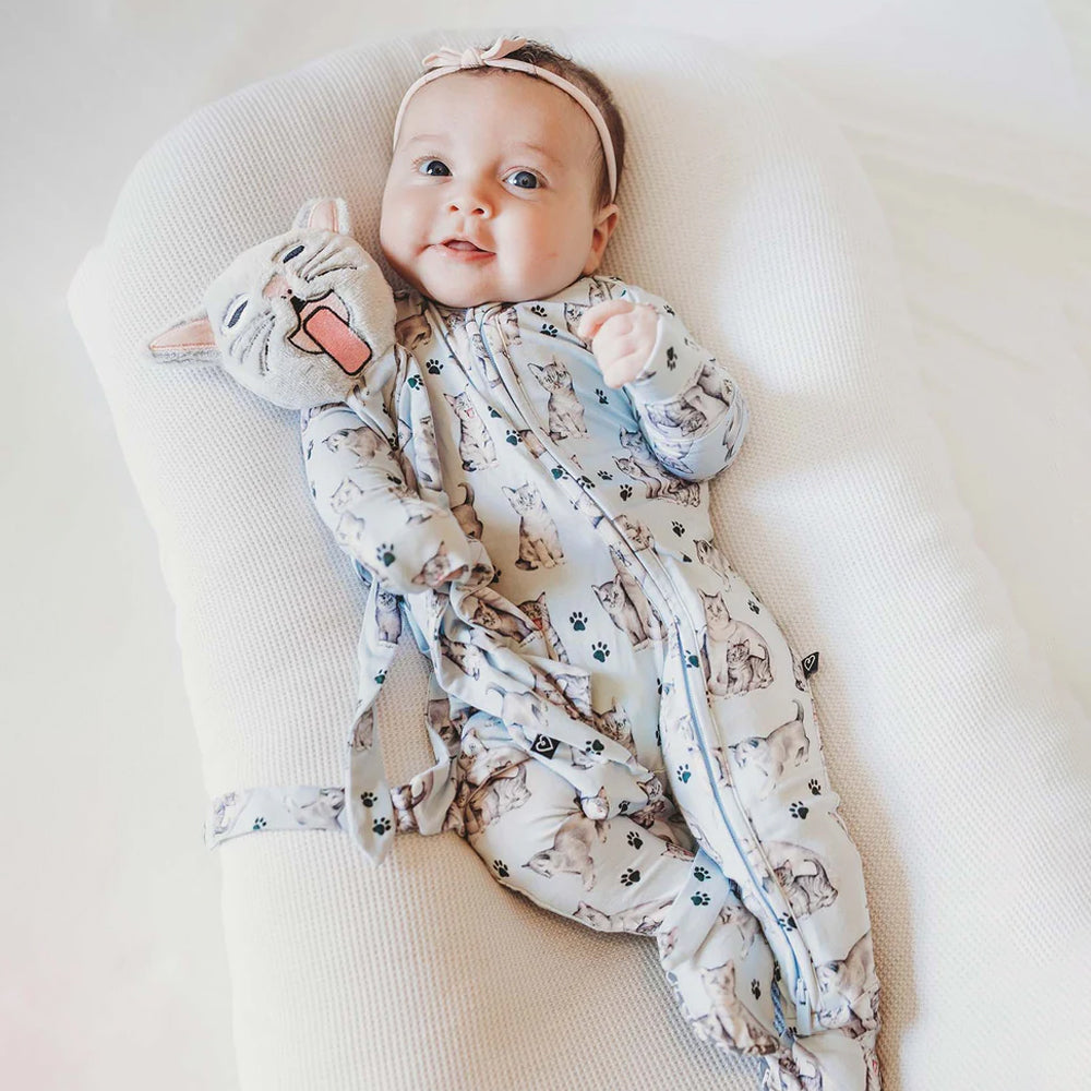 Baby wearing a patterned onesie with cat designs on a white surface