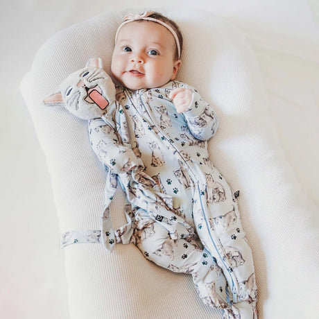 Baby wearing a patterned onesie with cat designs on a white surface
