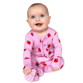 A baby wearing a pink long-sleeve footed sleeper with a strawberry print, sitting against a solid white background.