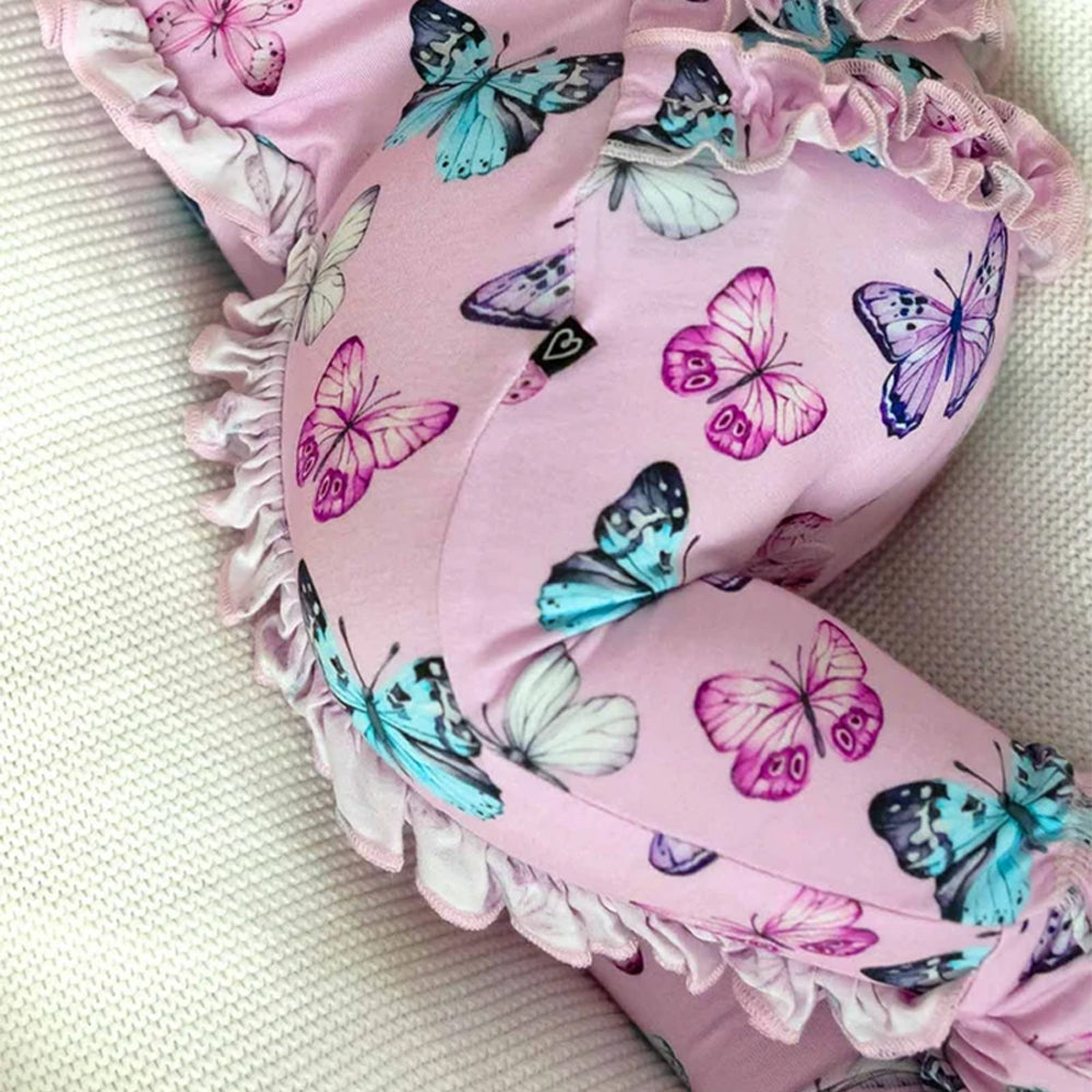 Pink baby bloomers with a colorful butterfly print and ruffled trim, laid flat on a textured white fabric background.