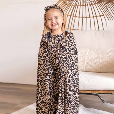 Child wearing a leopard print onesie standing in a room with a couch and decorative wall.
