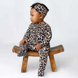 Child wearing a leopard print outfit sitting on a wooden stool against a white background