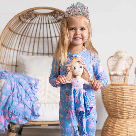 Young girl in princess-themed pajamas holding a doll, wearing a tiara, in a cozy room.