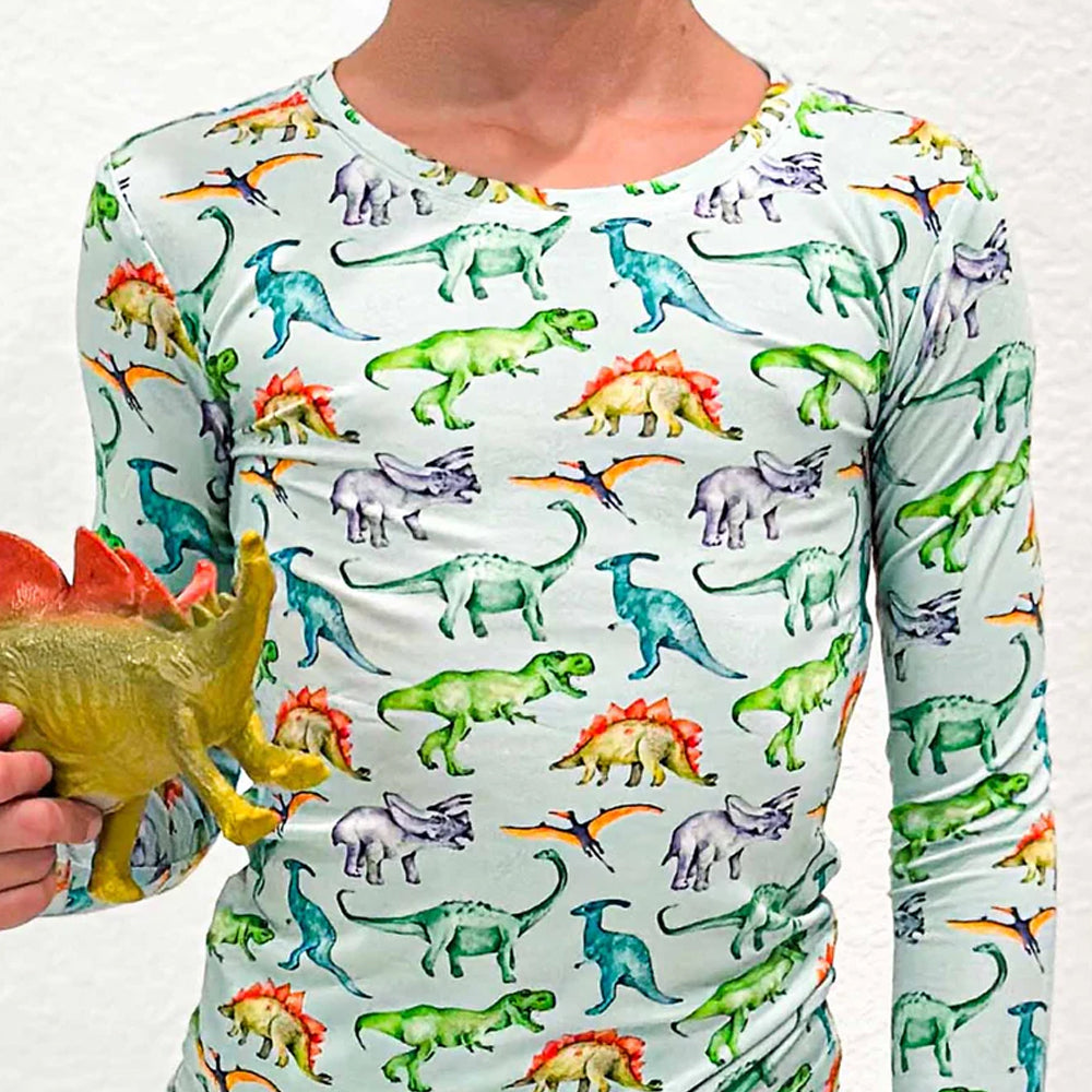 Person wearing a long-sleeve shirt with dinosaur pattern holding a toy dinosaur.