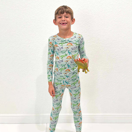 Child wearing a dinosaur-themed onesie holding a toy dinosaur against a white background