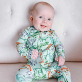 Baby wearing a dinosaur-patterned onesie sitting on a light-colored couch.