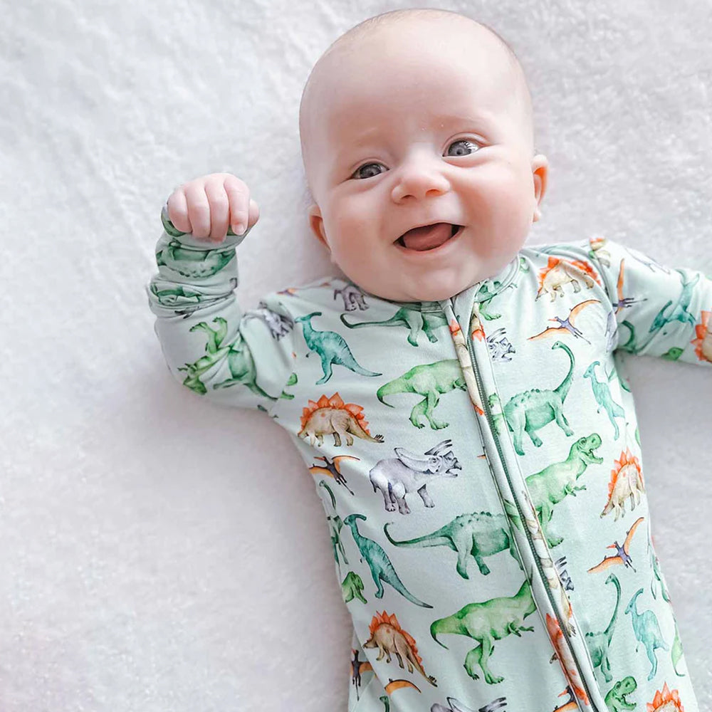 Baby wearing a dinosaur-patterned onesie on a white blanket