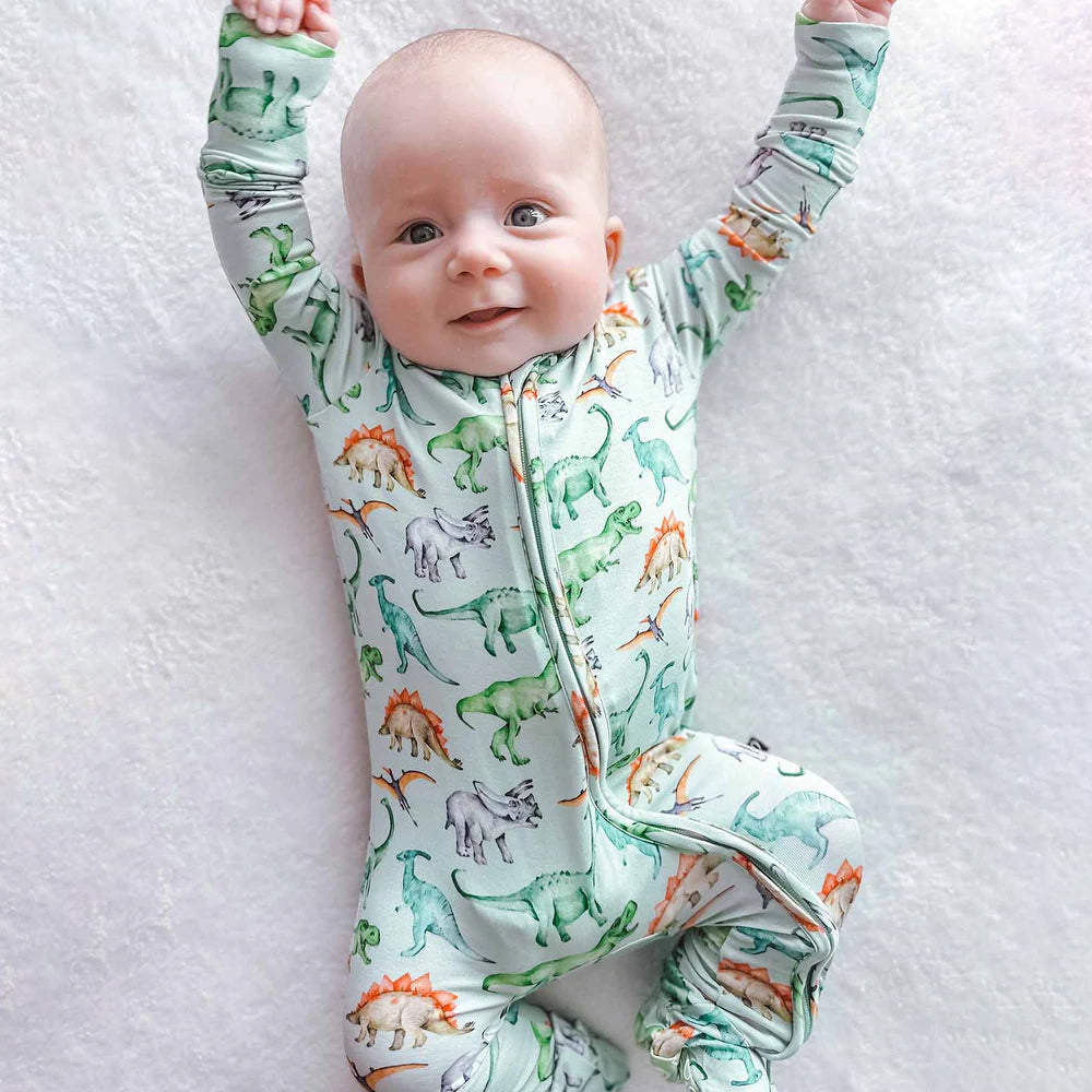 Baby wearing a dinosaur-patterned onesie on a white blanket