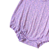 A close-up of a lavender ribbed fabric garment with a small pink and green floral print, showing the texture and snap-button closure at the bottom.