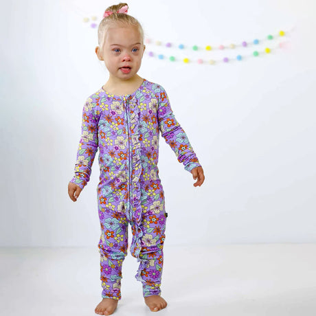 Child wearing a floral purple onesie against a white background