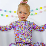 Child wearing a colorful floral onesie with a white background and decorative garland.