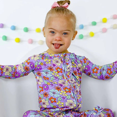 Child wearing a colorful floral onesie with a white background and decorative garland.