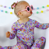 Child wearing a colorful floral outfit and pink sunglasses against a white background with colorful decorations.