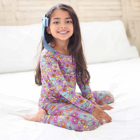 Young girl wearing a colorful floral pajama set on a bed.