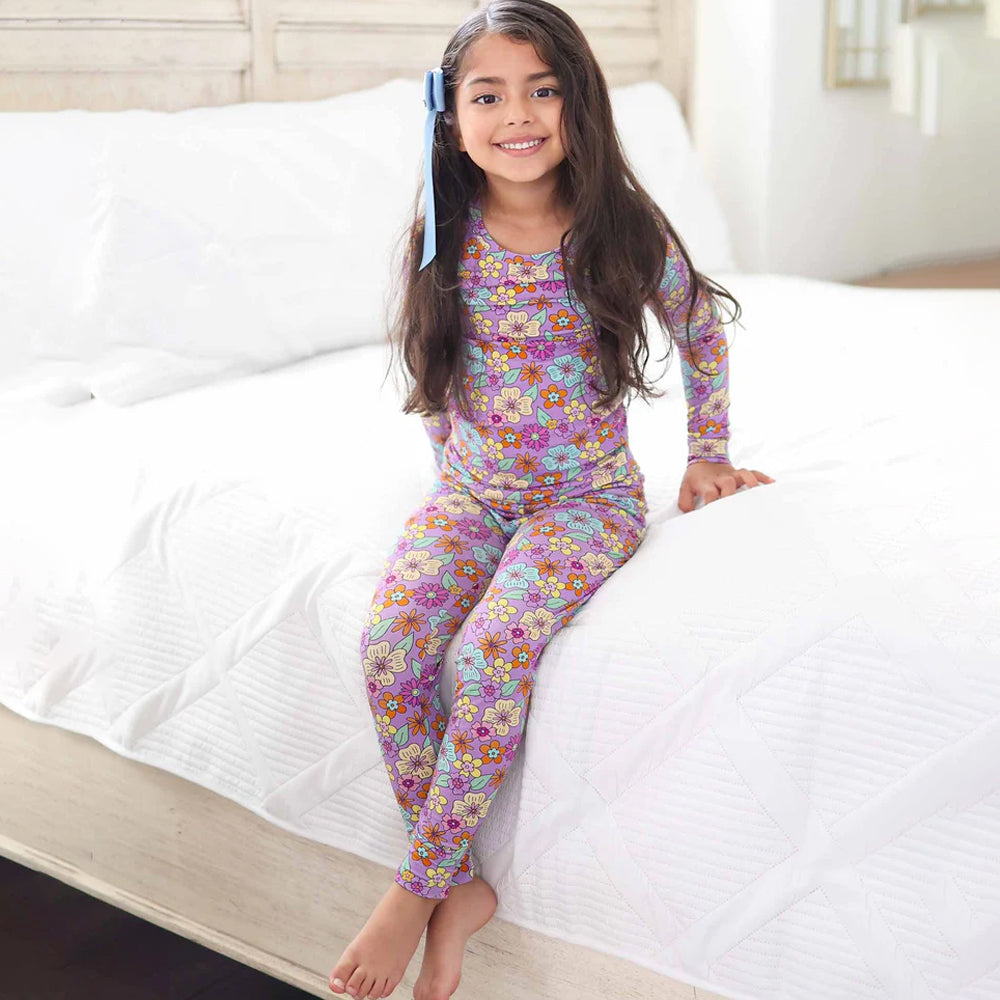 Young girl wearing a floral pajama set sitting on a bed.