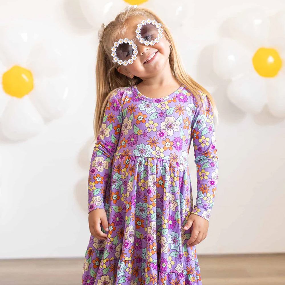 Child wearing a colorful floral dress with sunglasses in a bright room.