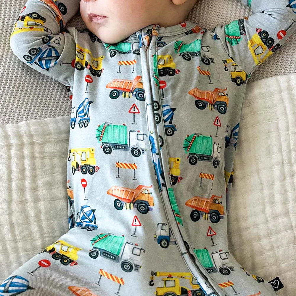 Baby wearing a onesie with construction vehicle pattern on a textured surface