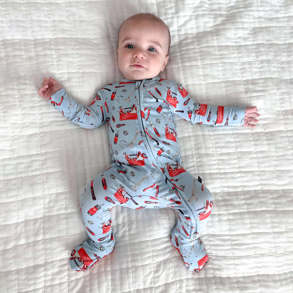 Baby wearing a gray onesie with red fox patterns on a striped bed.
