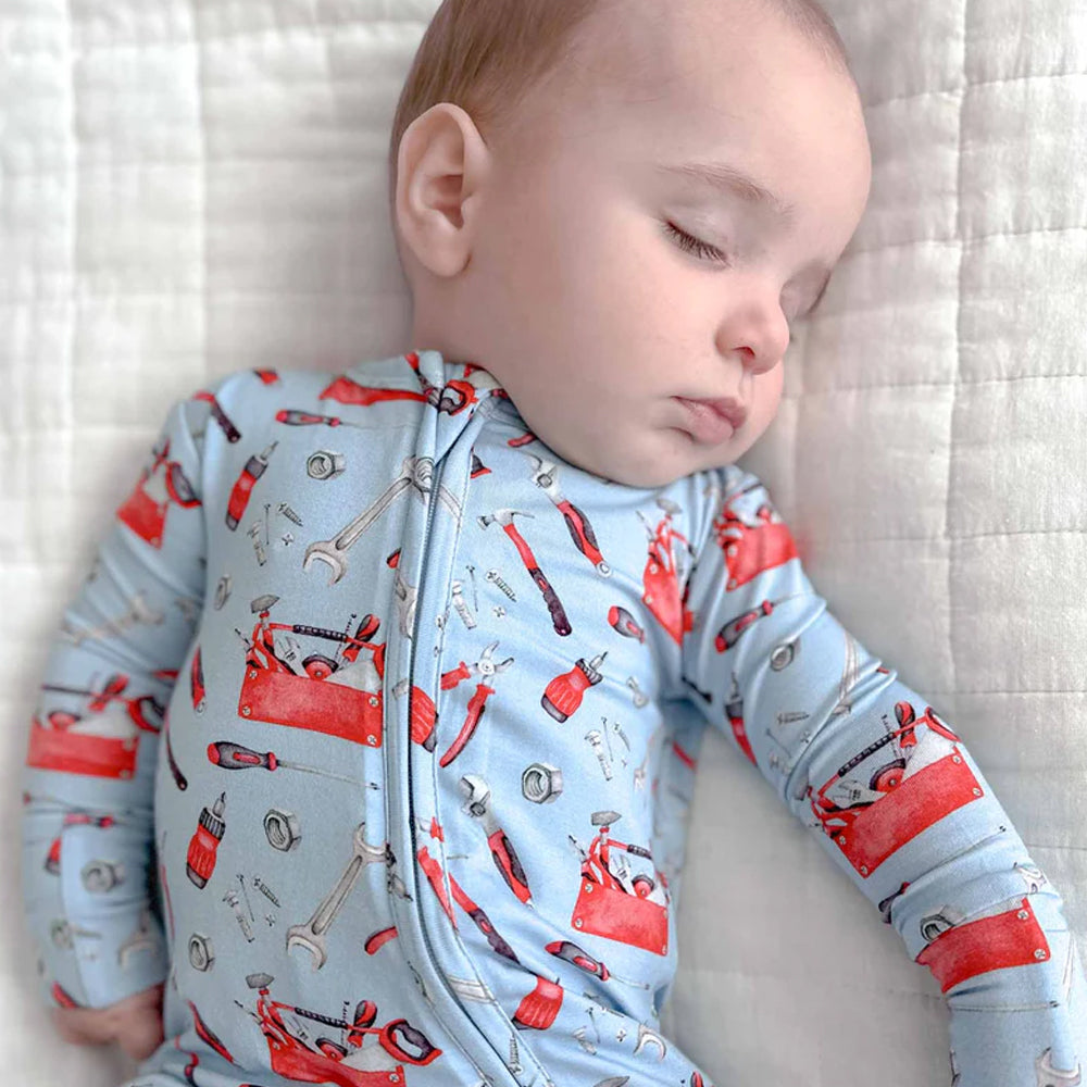 Baby wearing a onesie with tool design lying on a white blanket