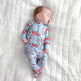 Baby wearing a blue onesie with red patterns, lying on a white textured surface.