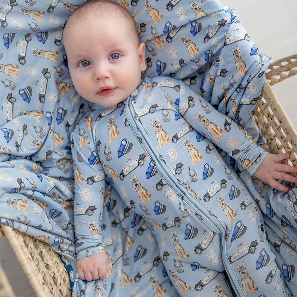 Baby in a crib with blue pajamas featuring animal and car patterns.