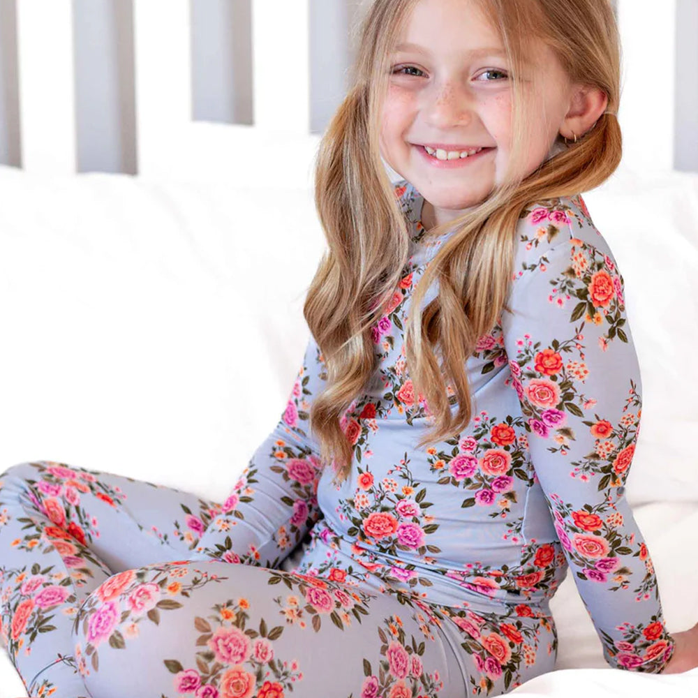 Young girl wearing a floral long-sleeve shirt and leggings sitting on a white surface.