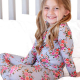 Young girl wearing a floral long-sleeve shirt and leggings sitting on a white surface.